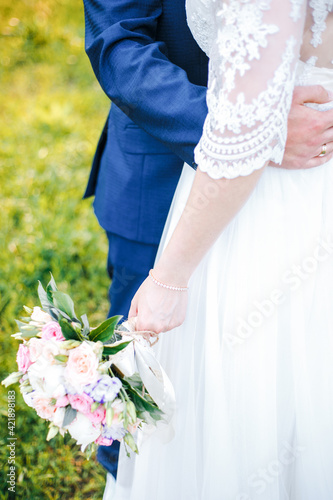 the bride holds a bouquet in her lowered hand, the groom hugs her waist