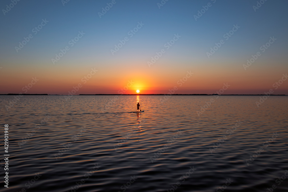Paddle boarder in the suns glow at sunset.