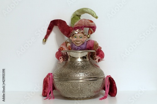 Foto buffoon toy holding silver shining jug on white background