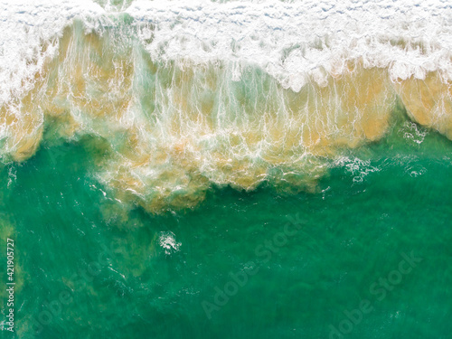 Aerial view of the sea with an emerald green color and large foaming waves
