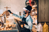 African American middle aged female worker with shield and protective mask on face working in bakery. Coronavirus, Covid-19 concept.