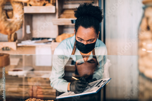 Bakery worker with face protective mask writes down orders for online delivery due to Coronavirus pandemic.