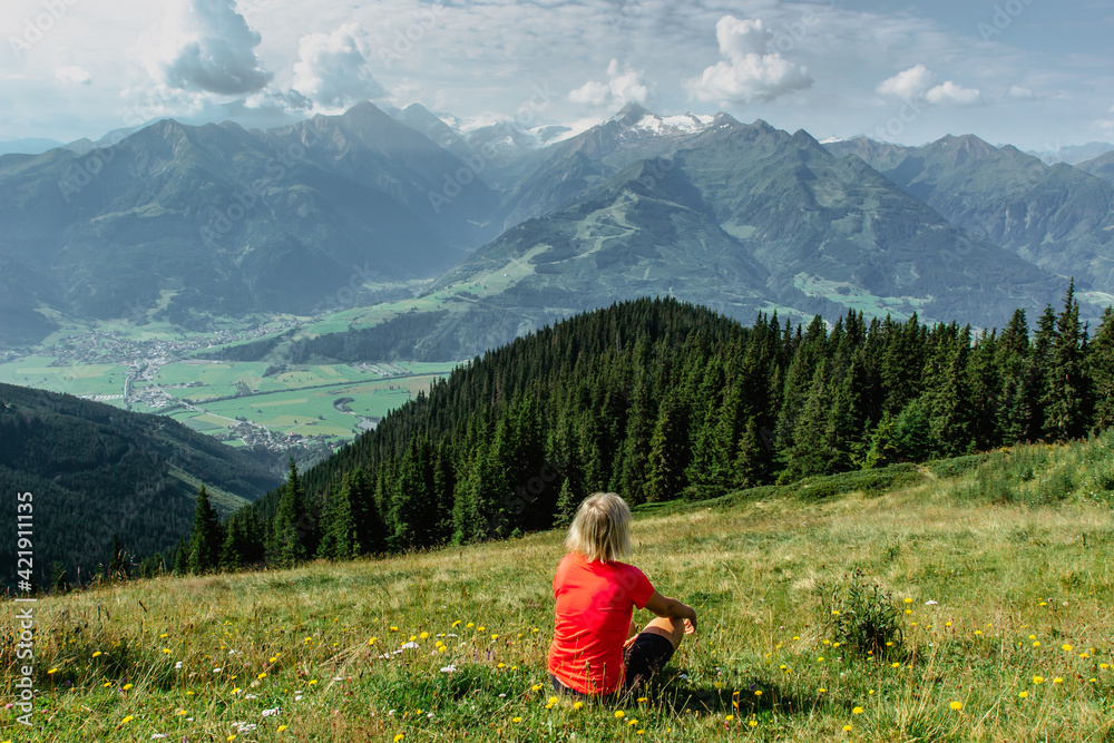 Blonde girl enjoying view during trekking in Alps, Austria.Majestic peaks of mountains,green meadows,view of valley. Active happy backpacker.Travel sport concept.Sitting relaxing female.Positive mood