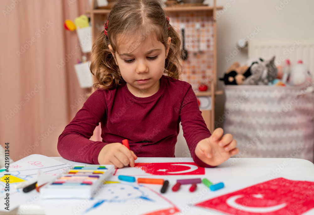 Fototapeta premium Portrait of small baby girl painting at home. Cute little child drawing Turkish flag picture. Turkish National Sovereignty and Children's Day or Commemoration of Atatürk Youth and Sports Day concept.