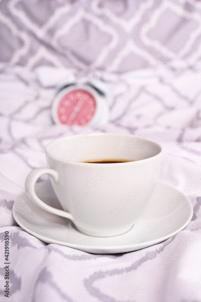 Coffee cup on modern bed sheets with alarm clock in the background