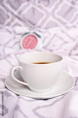 Coffee cup on modern bed sheets with alarm clock in the background