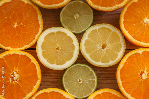 Oranges limes and lemons slides on wooden table view from above. Beautiful background with fresh fruit half cut.Healthy eating vitamin C.Summer tropical fruits food concept flat lay.