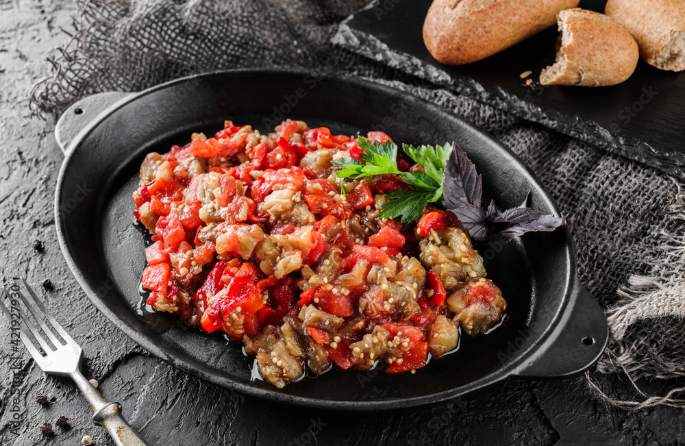 Delicious eggplant salad with pepper and tomatoes on large plate over dark background. Healthy vegan food, clean eating, top view Delicious eggplant salad with pepper and tomatoes on large plate over dark background. Healthy vegan food, clean eating, top view