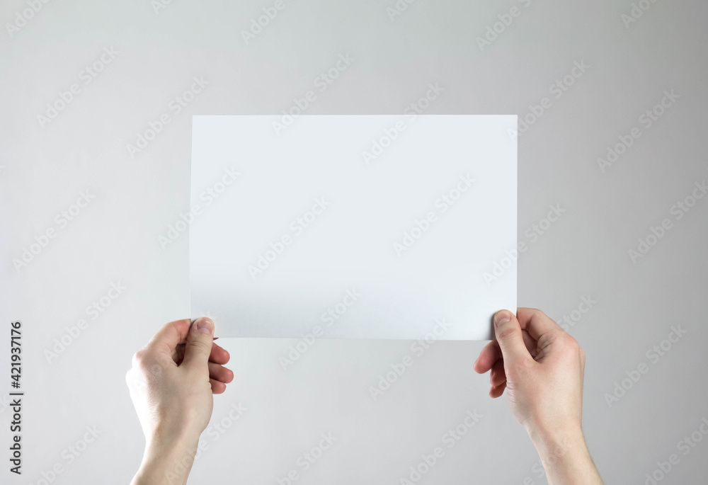 Hands hold an empty A4 sheet of paper. A clean flyer in your hands. For your text. Isolated on a gray background Hands hold an empty A4 sheet of paper. A clean flyer in your hands. For your text. Isolated on a gray background