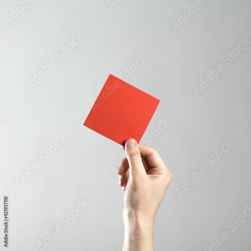 The hand holds an empty square red sheet of paper. A clean flyer in your hands. For your text. Isolated on a gray background