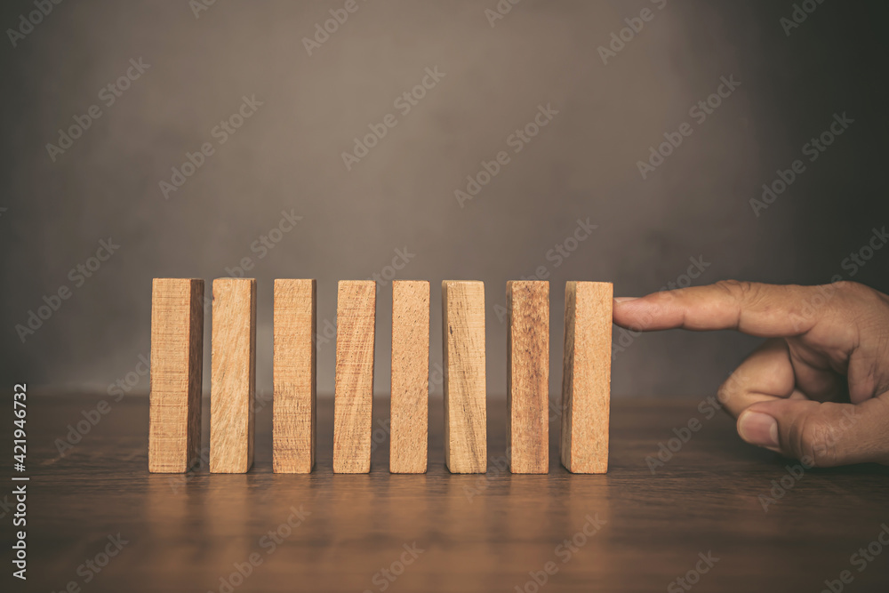Close-up fingers prevent the wooden block from falling domino concepts of financial risk management and strategic planning.