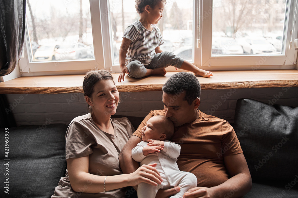 Woman hugging small newborn kid while sitting at the sofa with her husband Woman hugging small newborn kid while sitting at the sofa with her husband