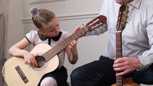 little girl and her father are playing guitar. Learning to play the guitar. Music education and extra-curricular lessons. © yavdat