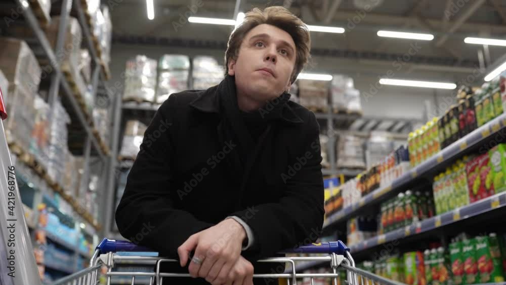 An angry man is standing in line at a supermarket with a cart