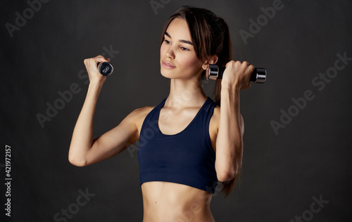 Sporty woman with dumbbells in her hands on a dark background smile emotions Copy Space