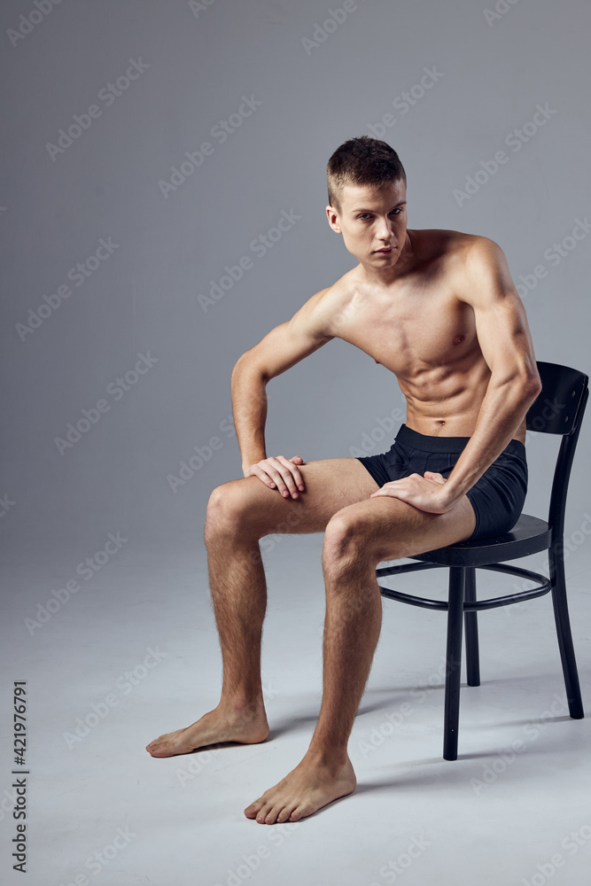 Fototapeta premium sporty man with a pumped up body in black shorts sits on a chair isolated background