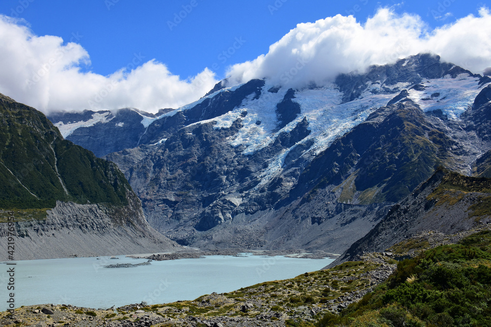 spectacular view of rugged mountain peaks and a glacial lake along the hooker valley track  on a sunny summer day, near mount cook village, on the south island of new zealand