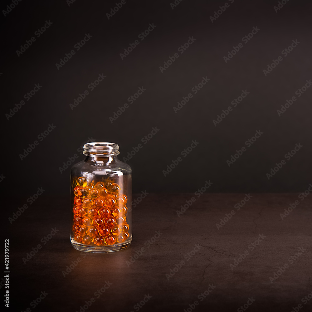 A glass jar with pills of bright orange yellow color on a brown background. A glass jar with pills of bright orange yellow color on a brown background.