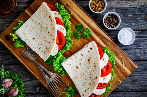 Italian piada wraps - piadina stuffed with fresh lettuce  mozzarella and sliced tomatoes on wooden table photo