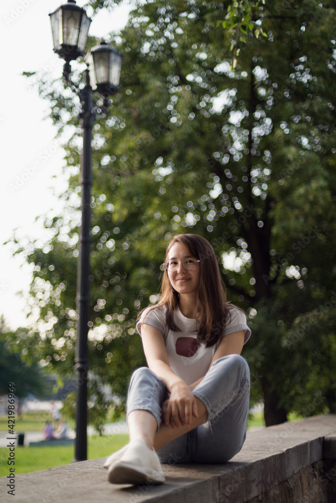 a beautiful Asian girl sits on the parapet against a background of green foliage a beautiful Asian girl sits on the parapet against a background of green foliage