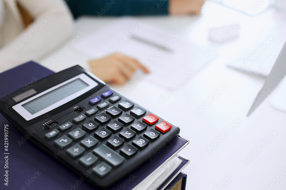 Calculator and binders with papers are waiting to be processed by business woman or bookkeeper working at the desk in office back in blur. Internal Audit and tax concept Calculator and binders with papers are waiting to be processed by business woman or bookkeeper working at the desk in office back in blur. Internal Audit and tax concept