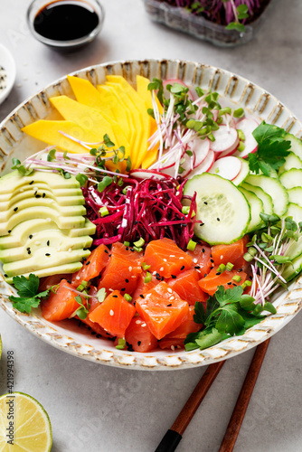 Poke bowl with fresh marinated salmon and variegated vegetables, green onions and microgreens. Gray background