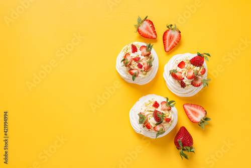 Perfect Pavlova with whipped mascarpone cream and fresh strawberry slices, sprinkled with crushed pistachios.Yellow background. top view photo