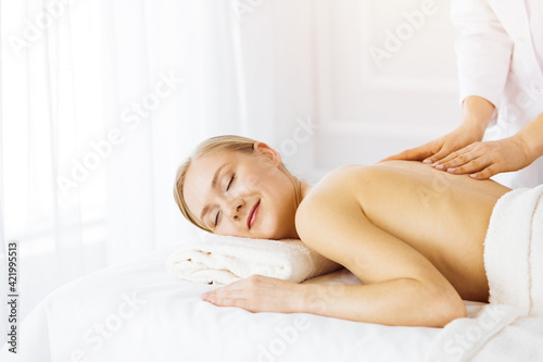 Beautiful caucasian woman enjoying back massage with closed eyes in sunny Spa salon