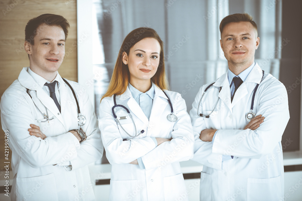 Group of modern doctors standing as a team with arms crossed in hospital office. Physicians ready to examine and help patients. Medical help, insurance in health care, best treatment and medicine Group of modern doctors standing as a team with arms crossed in hospital office. Physicians ready to examine and help patients. Medical help, insurance in health care, best treatment and medicine