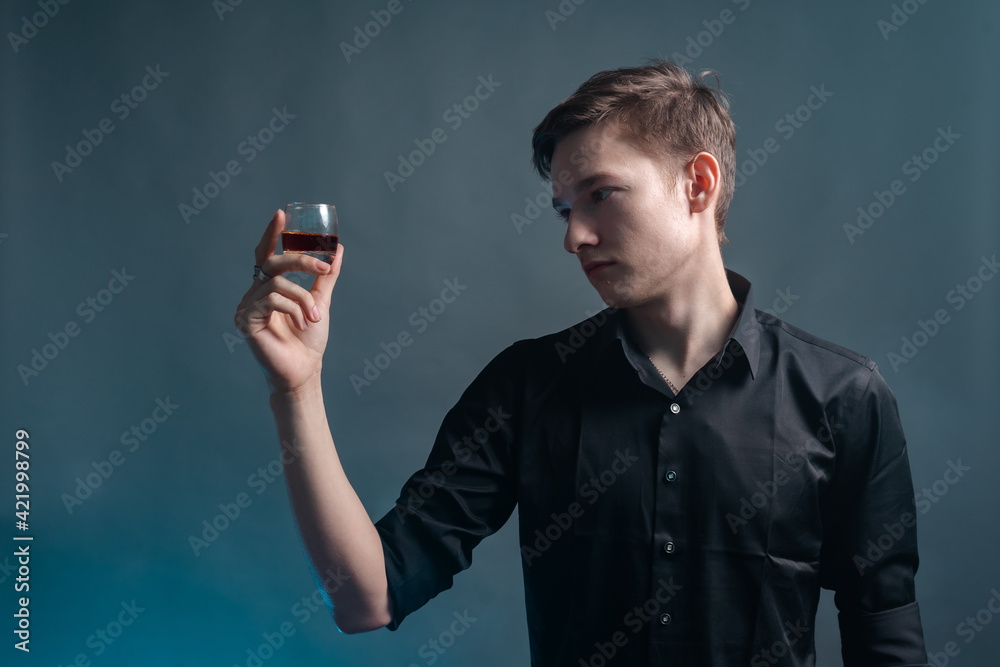 A young man holds a glass of rum on a gray background A young man holds a glass of rum on a gray background
