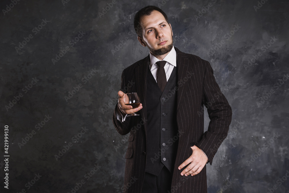 Bearded man in elegant suit holds a cognac glass on the abstract blurred background Bearded man in elegant suit holds a cognac glass on the abstract blurred background