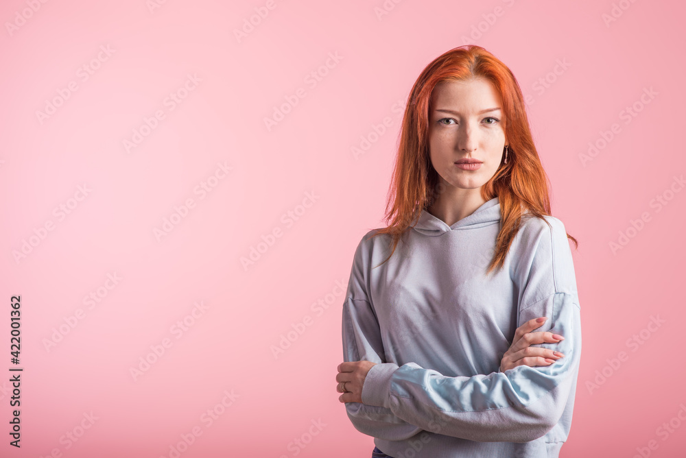 Obraz premium Portrait of a redhead girl who crossed her arms in the studio on a pink background with copyspace