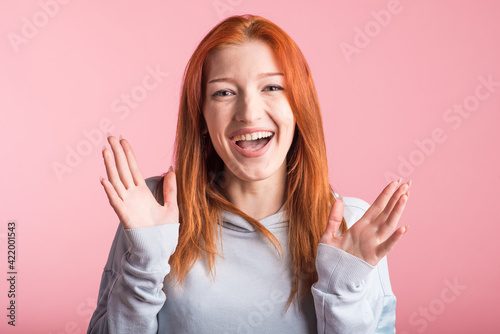 Excited redhead girl in studio on pink background