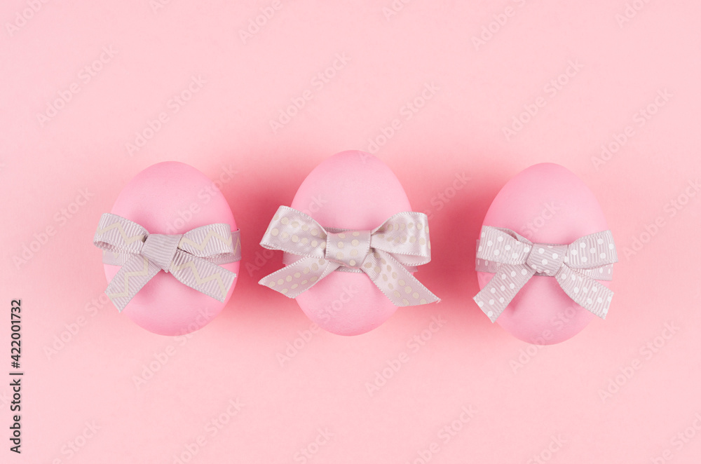 Pink easter eggs with grey bows in row on pastel pink background, top view.
