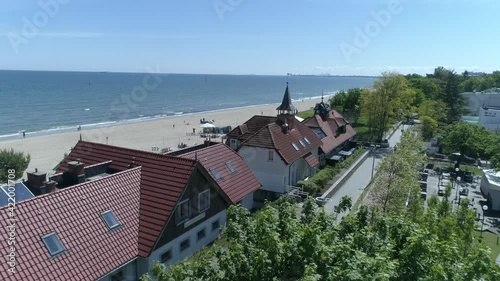 A drone view of the sea and wide, sandy beaches. On the first plan there is a promenade with a bicycle path as well as hotel and gastronomic buildings. Beautiful sunny weather with blue sky.
