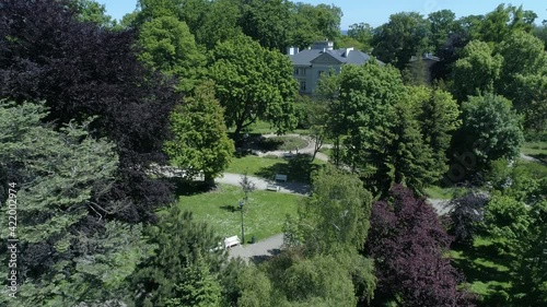 Lots of colorful trees located in the seaside park. Drone video captured on a sunny summer day with a blue sky. There are numerous alleys and benches in the park.