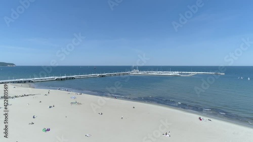 Pier in Sopot, Poland, visible on the video from the drone. In the foreground a sandy beach with people relaxing. In the background, the Baltic Sea and the famous pier on it.