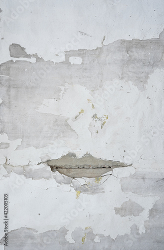 Cracks on wall looking like a mouth shape showing grey concrete.   Old white paint is peeling off.  Building,  construction, renovation, background categories.