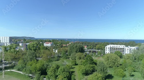 Sopot in Poland on a video from a drone. In the foreground a park with lots of green trees. Few city buildings and in the background the Baltic Sea and the famous Sopot Pier.