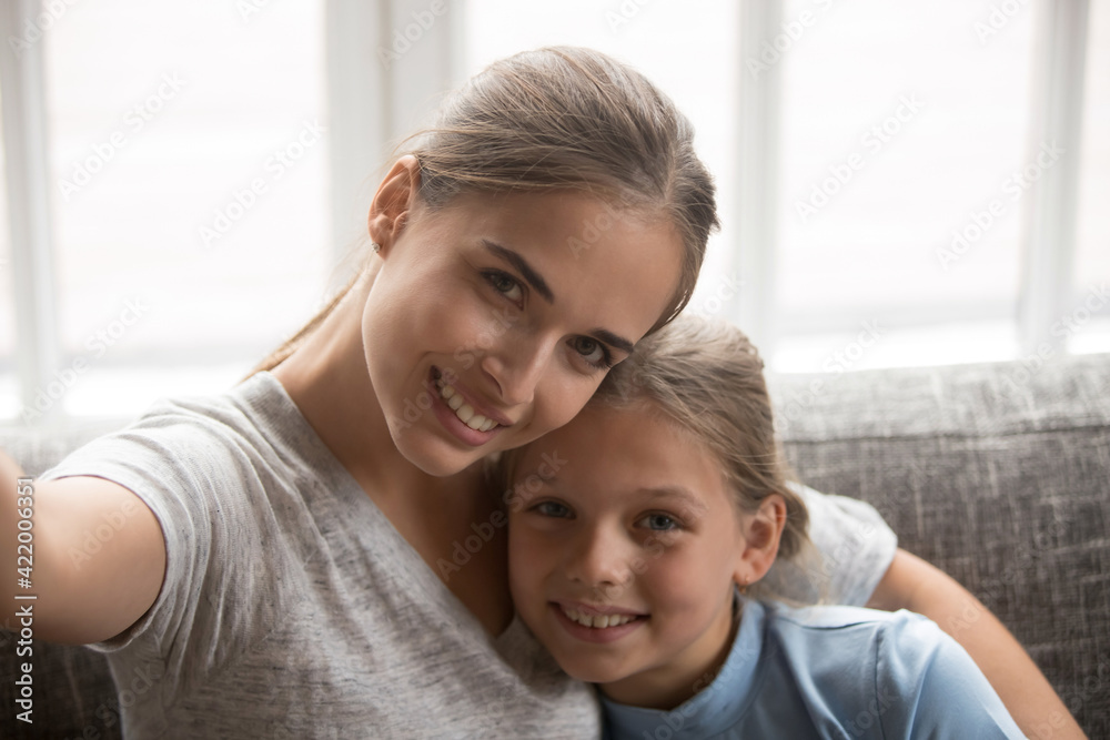 Smiling young Caucasian mother and small teen daughter make self-portrait picture on smartphone. Happy mom and little girl child have fun pose for family selfie on cellphone. Technology concept. Smiling young Caucasian mother and small teen daughter make self-portrait picture on smartphone. Happy mom and little girl child have fun pose for family selfie on cellphone. Technology concept.