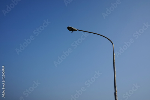 An electric lamp post has a broken light with some materials hanging. The street light is left abandoned. Objects, industrial maintenance categories.