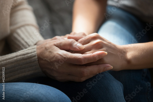 Crop close up of mature mother and adult daughter hold hands talk share secrets show love and care in family relations. Supportive senior mom comfort caress upset grownup child. Support concept.