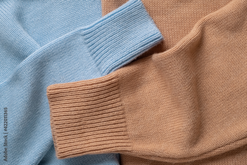 Two sleeves of woolen women's sweaters in soft blue and beige colors. Two sleeves of woolen women's sweaters in soft blue and beige colors.