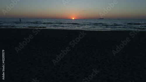Drone flight over the beach and sea at sunrise. Sandy beach, rippling water and a beautiful orange sun on the horizon.