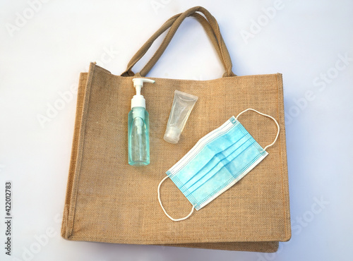 An alcohol pump, a hand gel sanitizer and a face mask are on a hemp bag. All items are important for people during Covid 19 pandemic. 
