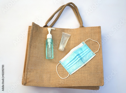 An alcohol pump, a hand gel sanitizer and a face mask are on a hemp bag.  All items are important for people during Covid 19 pandemic.  
