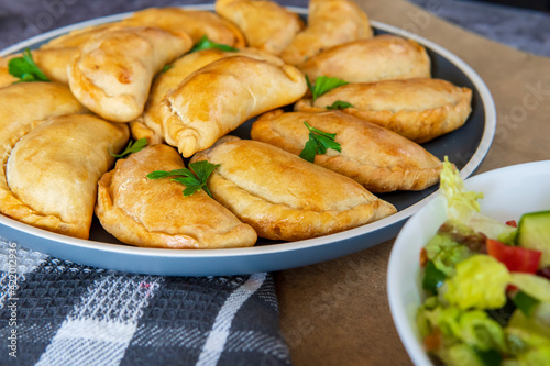 Empanadas - traditional Latin American baked beef pastry on a plate with a fresh salad sidedish. Gluten free savory appetizer with meat stuffing or filling. Handmade typical dish in Spain or Argentina
