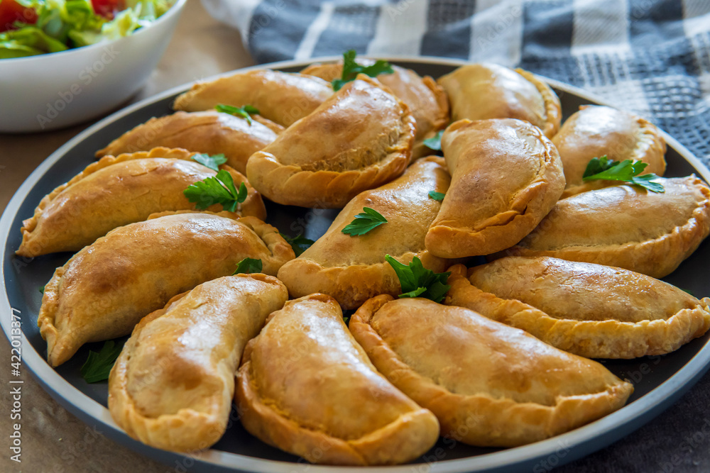 Traditional Latin American baked beef empanadas on a plate with a fresh salad sidedish. Gluten free savory pastries with meat stuffing or filing. Handmade typical dish in Spain or Argentina. Close up