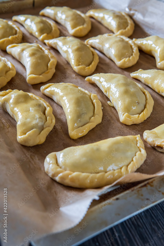 Uncooked empanadas on a baking tray. Traditional Latin American baked beef pastry ready for the oven. Gluten free savory appetizer with meat filling. Handmade typical dish in Spain or Argentina. Side 