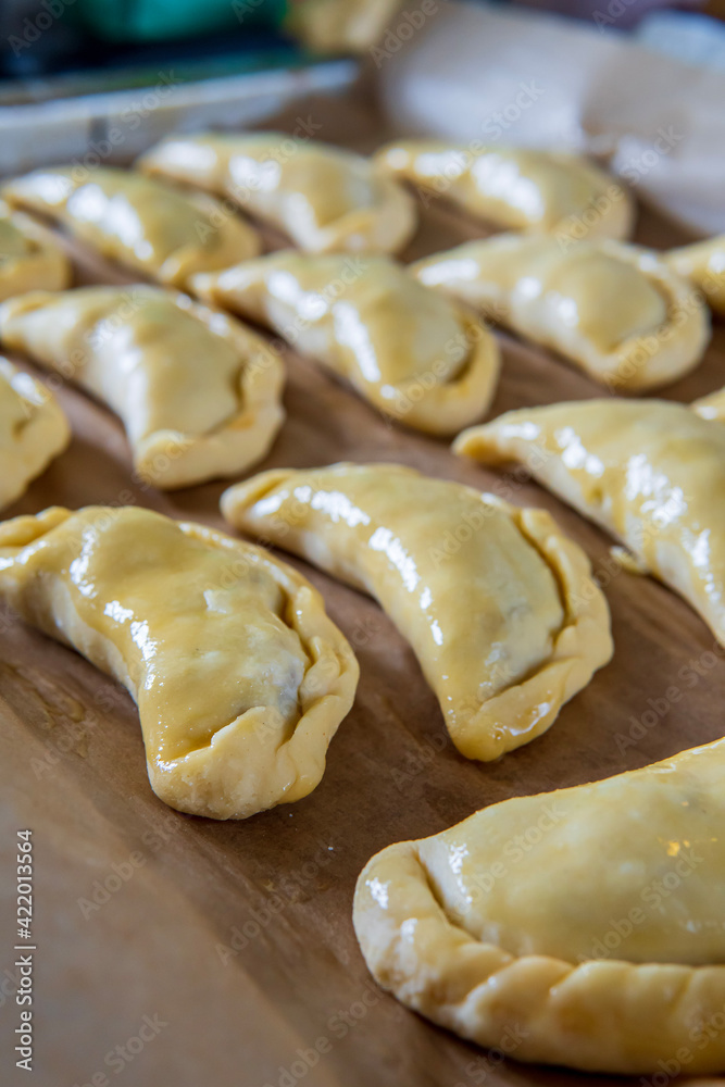 Uncooked empanadas on a baking tray. Traditional Latin American baked beef pastry ready for the oven. Gluten free savory appetizer with meat filling. Handmade typical dish in Spain or Argentina. Side Uncooked empanadas on a baking tray. Traditional Latin American baked beef pastry ready for the oven. Gluten free savory appetizer with meat filling. Handmade typical dish in Spain or Argentina. Side